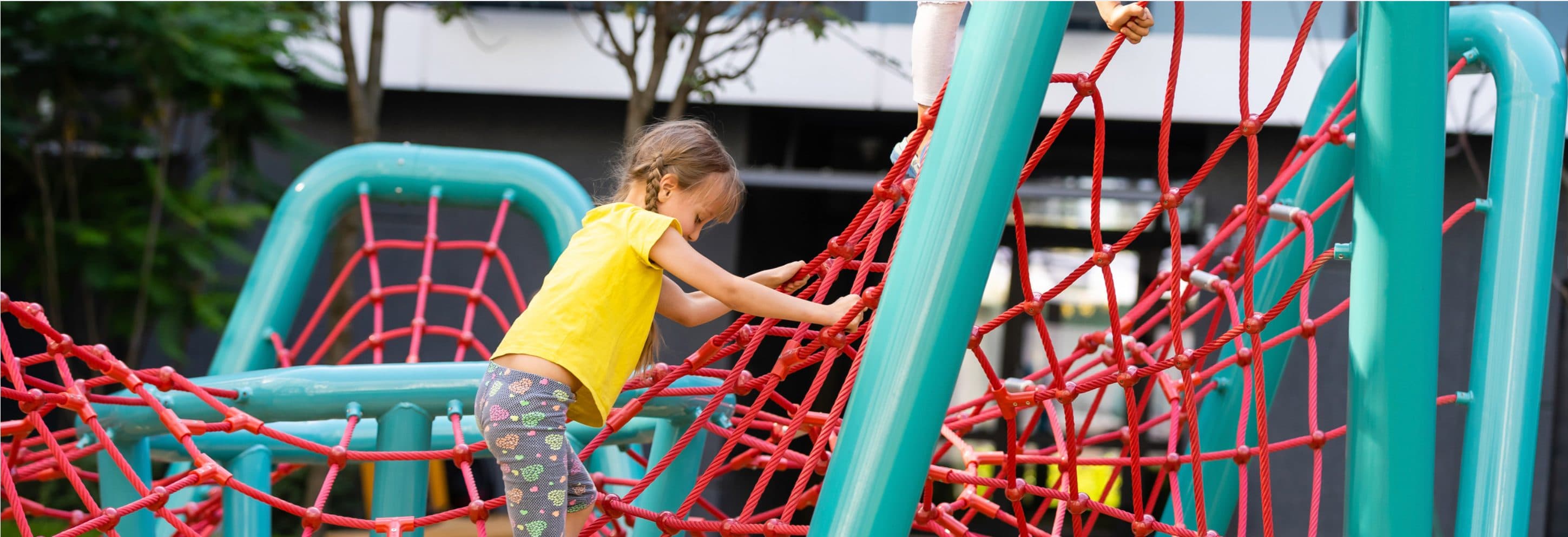 Child climbing a red rope net on teal steel playground posts